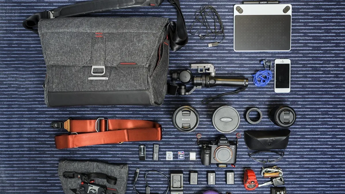 A collection of various items, including a gray bag, a tablet, a phone, a camera, a wallet, a watch, a pair of glasses, a pen, a pencil, a notebook, a small bag, a strap, a lens cap, a battery pack, a charger, a cable, a small bag, a pouch, a small bag, a small bag, a small bag, a small bag, a small bag, a small bag, a small bag, a small bag, a small bag, a small bag, a small bag, a small bag, a small bag, a small bag, a small bag, a small bag, a small bag, a small bag, a small bag, a small bag, a small bag, a small bag, a small bag, a small bag, a small bag, a small bag, a small bag, a
