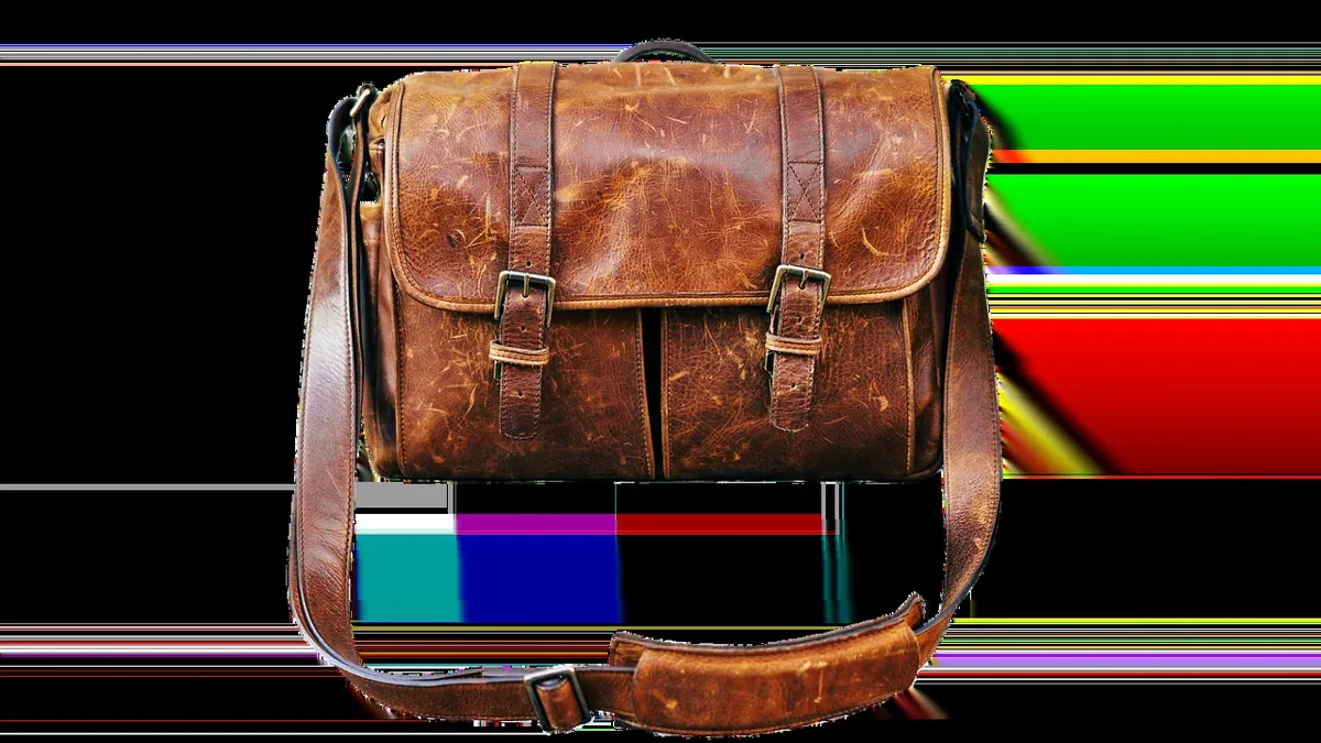 A brown leather satchel with a strap and buckle, placed on top of a colorful object that is partially visible.