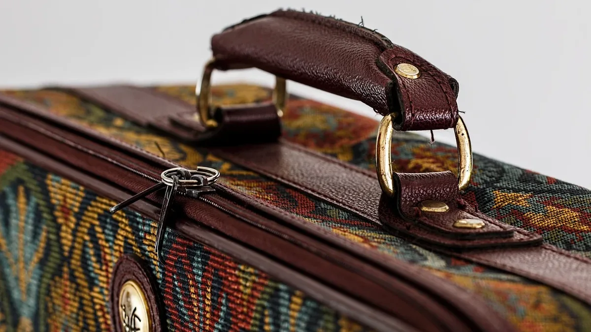 A close-up of a brown leather handle on a colorful fabric bag with a zipper and a metal clasp.