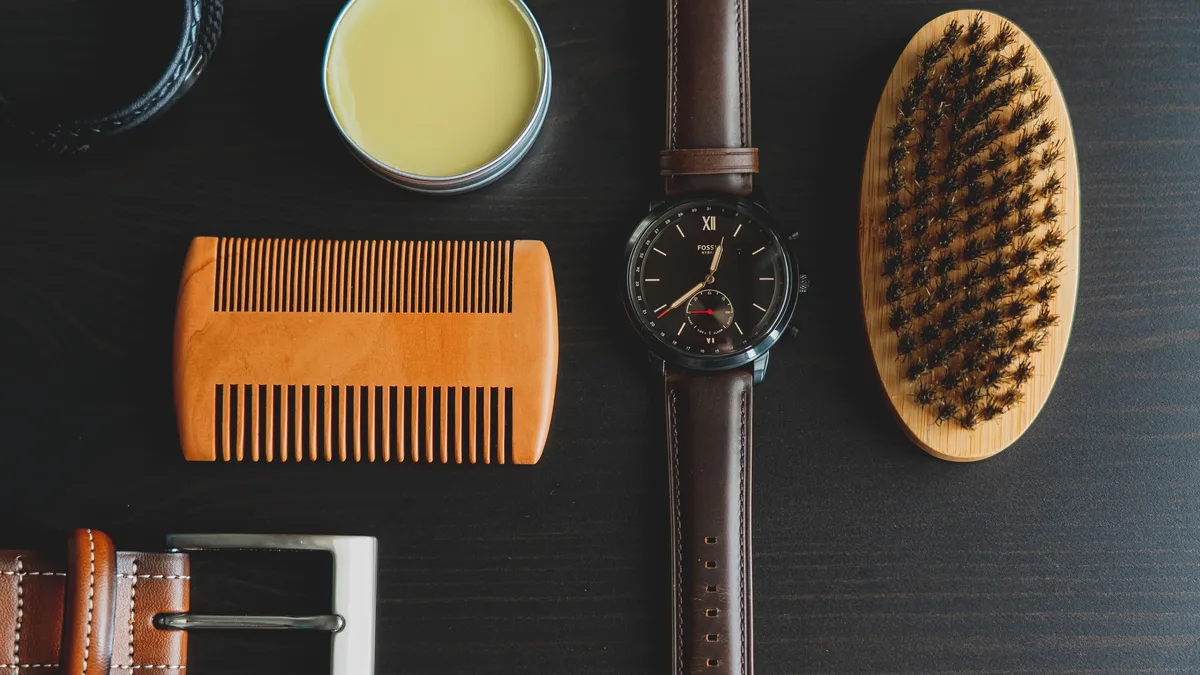 A collection of grooming and accessory items, including a comb, a watch, a belt, a brush, and a tin of cream, arranged on a dark surface.